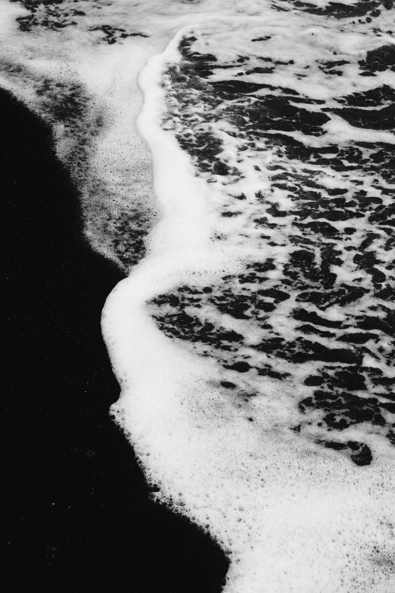 Zwart-witte schuimlijn op donker strand